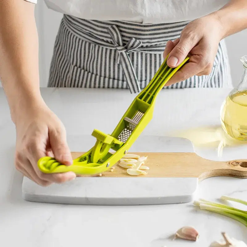 2-in-1 Garlic Press and Slicer, Green Options being used to slice garlic on a wooden cutting board.