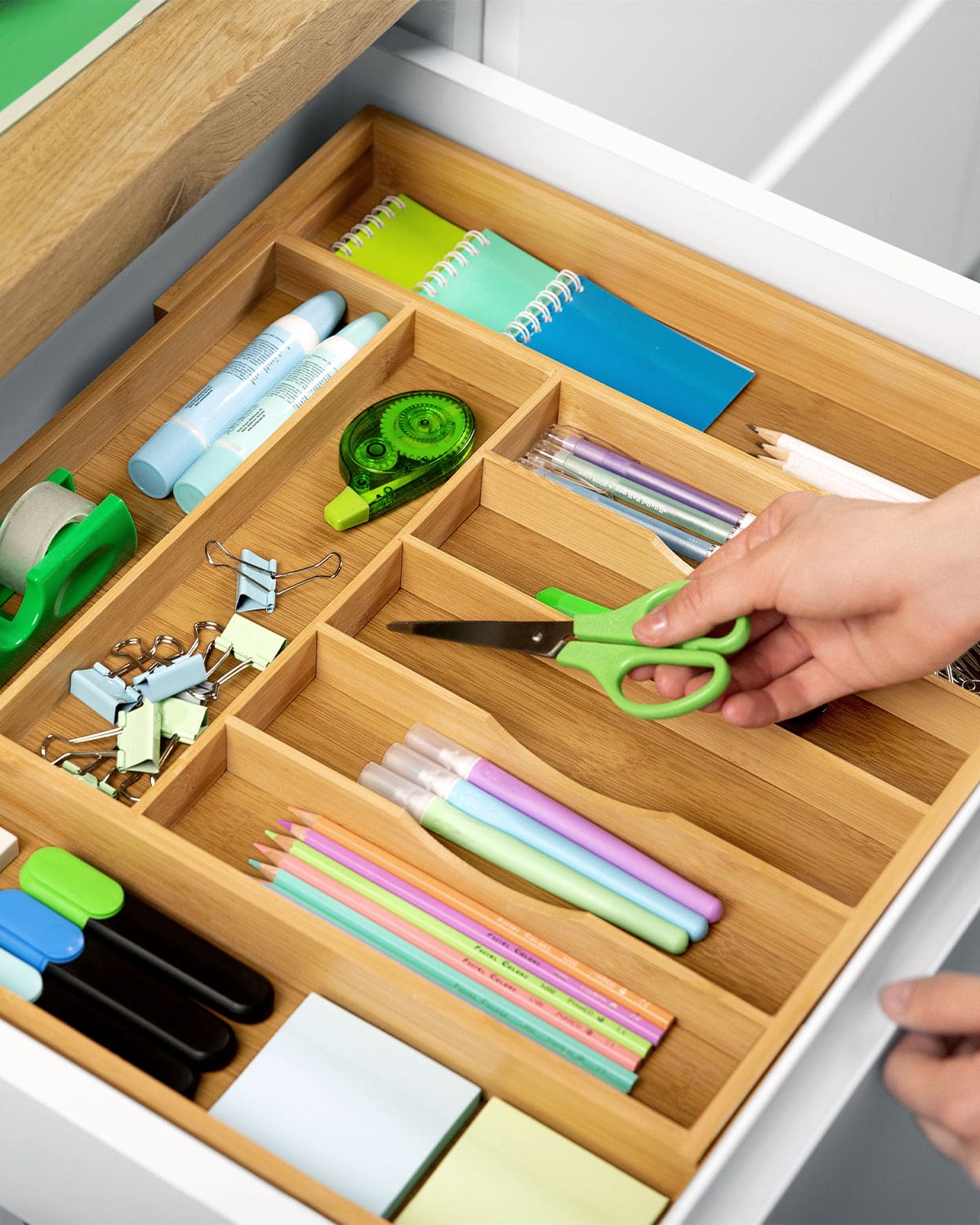 expandable bamboo drawer organizer with 9 slots holding office supplies, scissors, pens, and notebooks in an open drawer