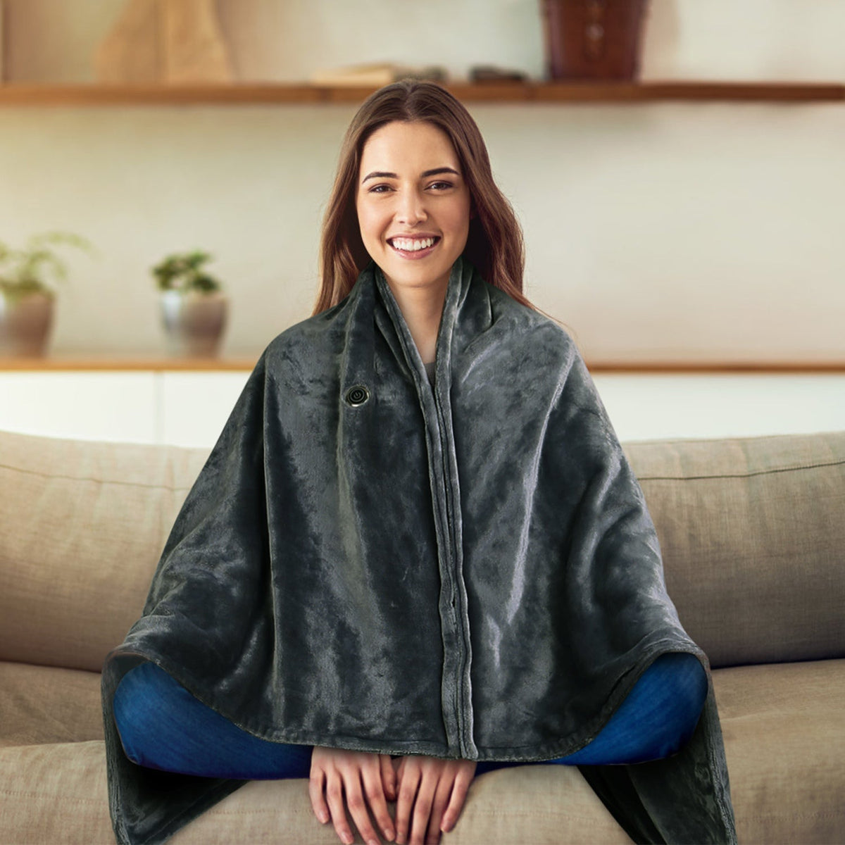 Woman wearing USB heated wearable blanket wrap in charcoal gray with zipper, hands free while sitting on couch