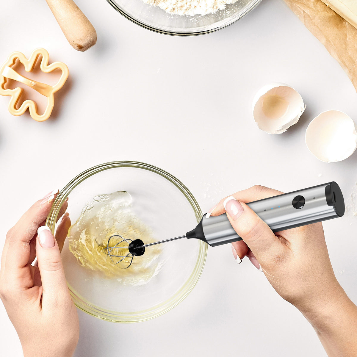 rechargeable handheld milk frother with silver handle whisking cream in glass bowl, kitchen setting