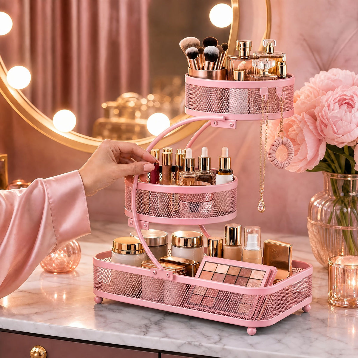 Pink 3-tier metal bathroom organizer with hooks holding makeup, brushes, and skincare on vanity