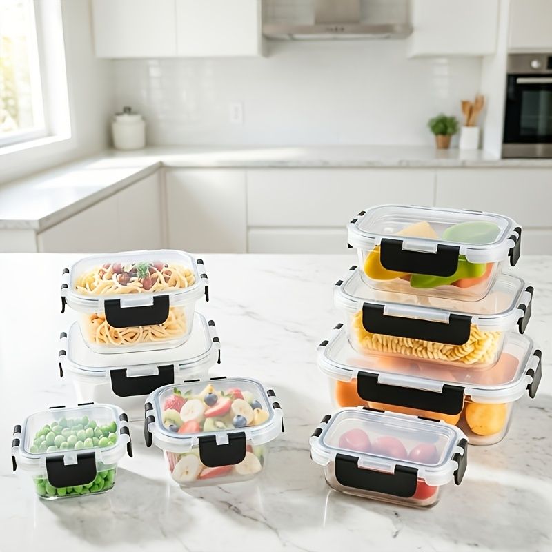 Glass food storage containers with lids stacked on marble counter displaying various meal prep foods in modern white kitchen