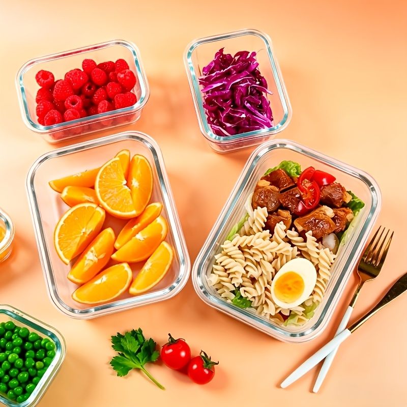Glass food storage containers with lids filled with fresh raspberries, red cabbage, orange slices, and pasta meal prep