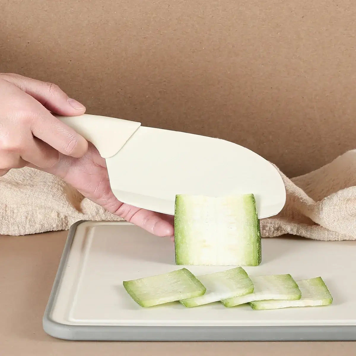 5-piece kitchen knife set with scissors cutting fresh vegetables on a countertop with a light-colored knife and green cucumber slices.