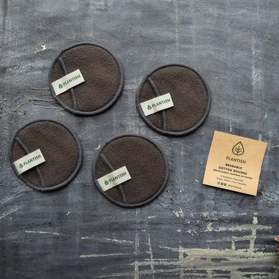 Set of 4 reusable bamboo charcoal cotton rounds with branded tags, displayed with kraft packaging on textured surface