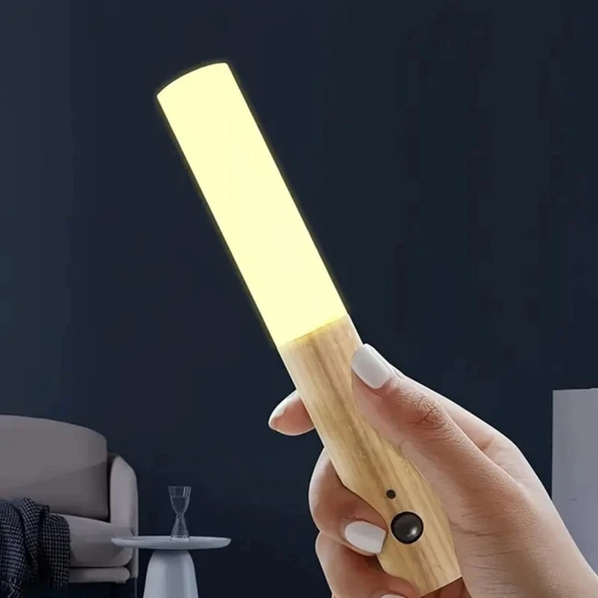 Rechargeable motion sensor night light with wood handle held in hand, glowing in dark bedroom setting