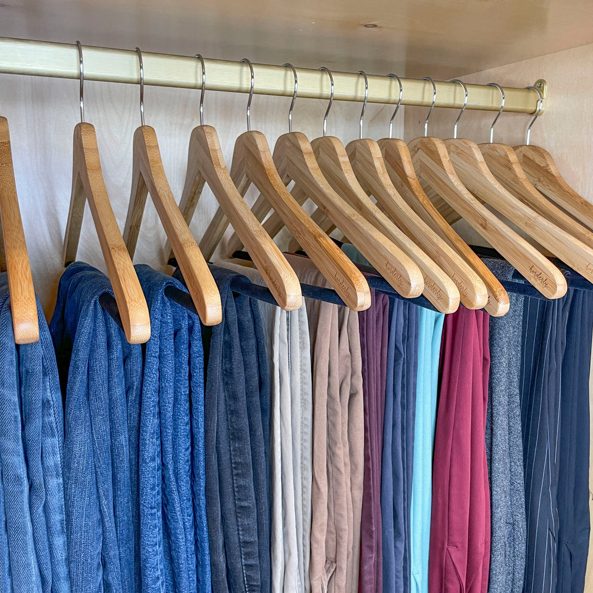 Row of matching bamboo hangers holding pants in a closet