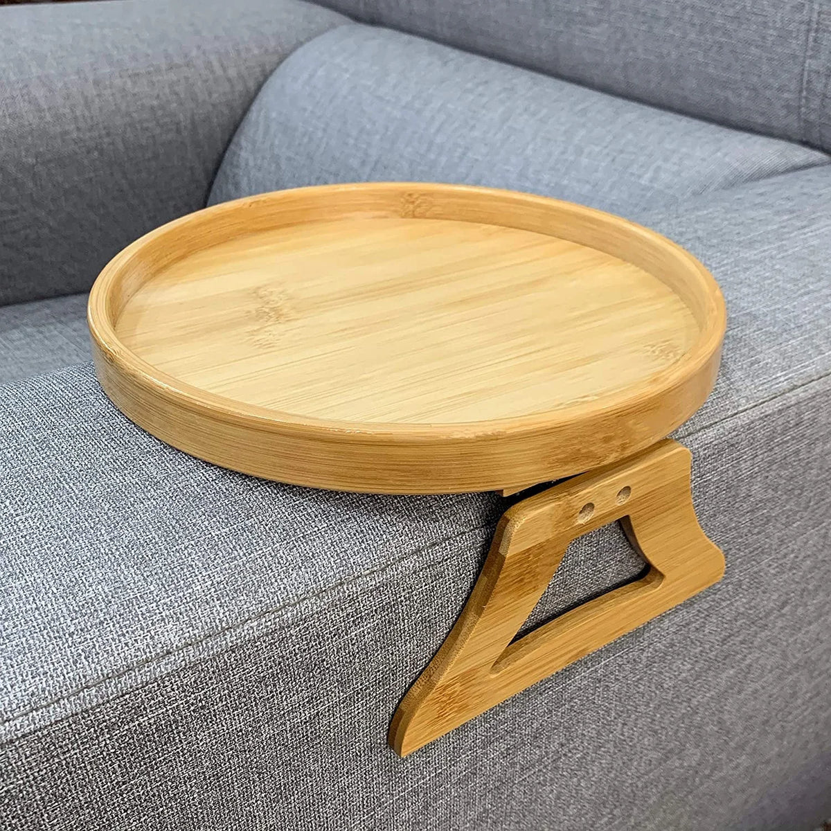 Round bamboo armrest tray clipped onto a gray sofa arm.