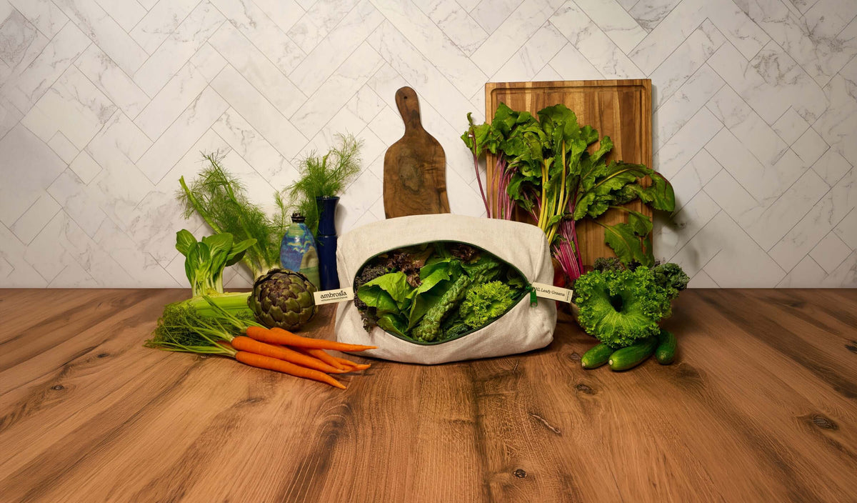 extra large leafy greens storage bag surrounded by fresh vegetables on a wooden countertop.