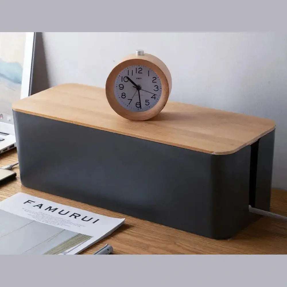 Bamboo cable organizer box on a desk with a clock and notebooks for organized storage of cables and wires.