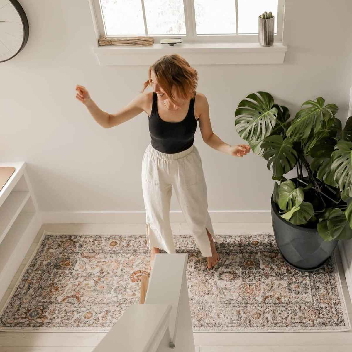 A woman dancing on a Herstmonceux elegant area rug surrounded by indoor plants.