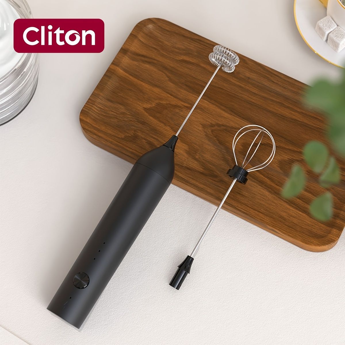 Black rechargeable handheld milk frother with 2 whisk heads displayed on wooden board