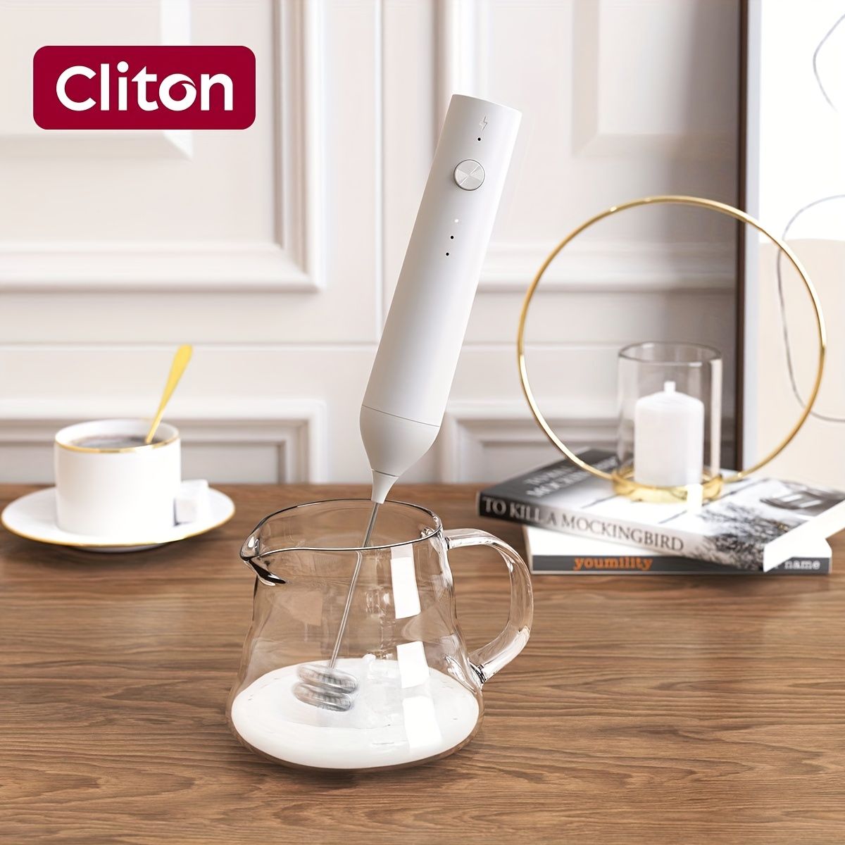 White rechargeable handheld milk frother with speed control frothing milk in glass pitcher on wooden table