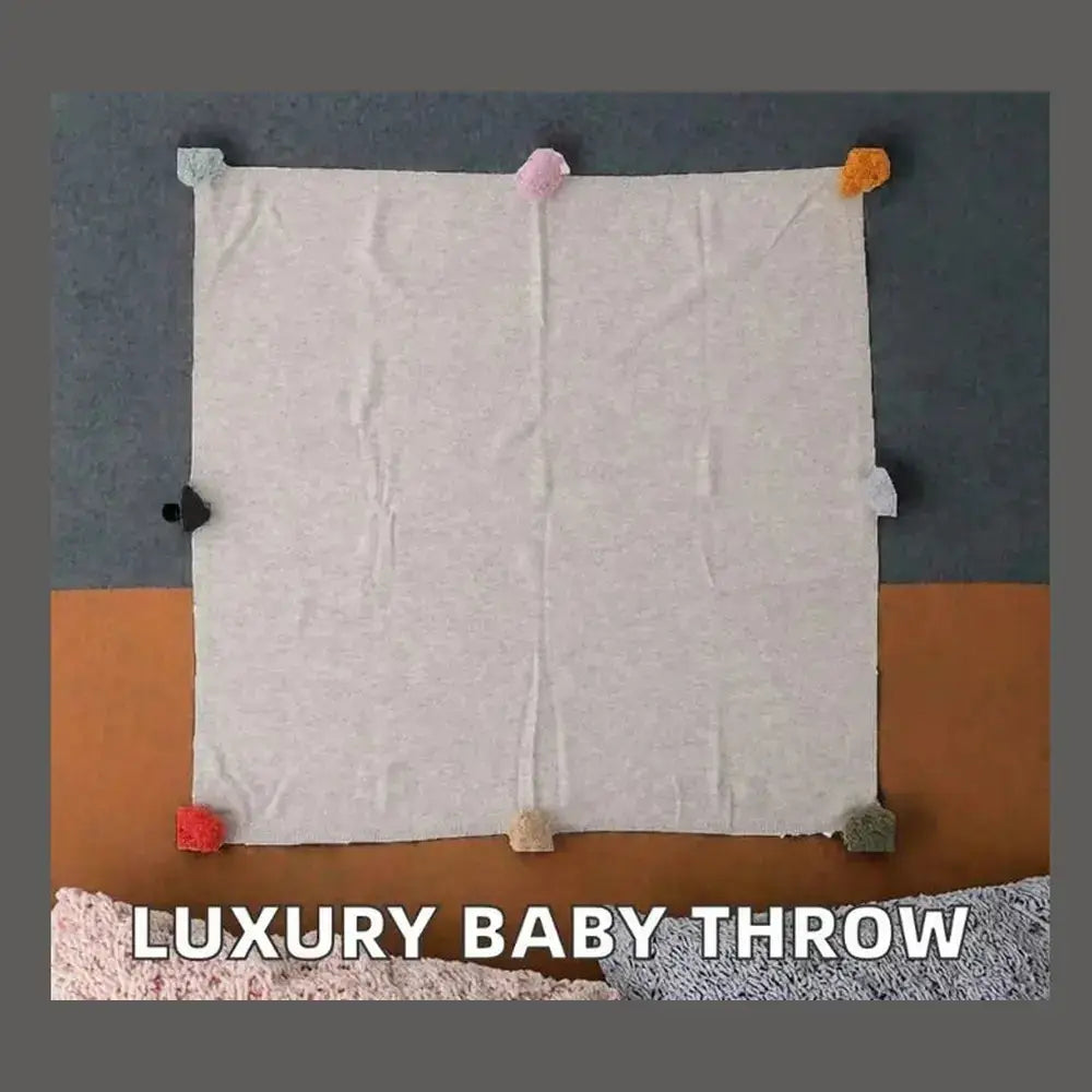 Luxury cashmere throw blanket in soft gray with colorful pom-poms, perfect for cozy evenings.