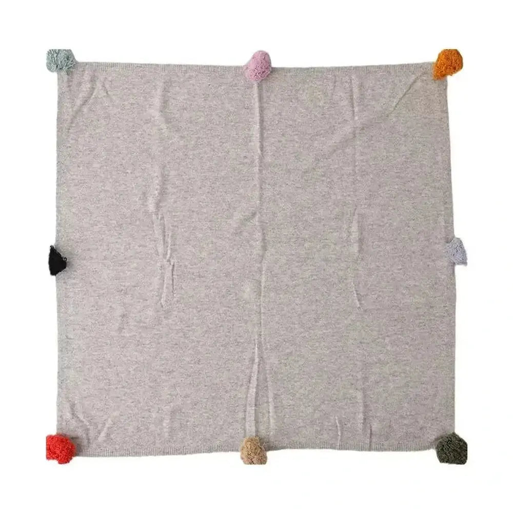 Luxury cashmere throw blanket with colorful pom-poms, perfect for cozy evenings.