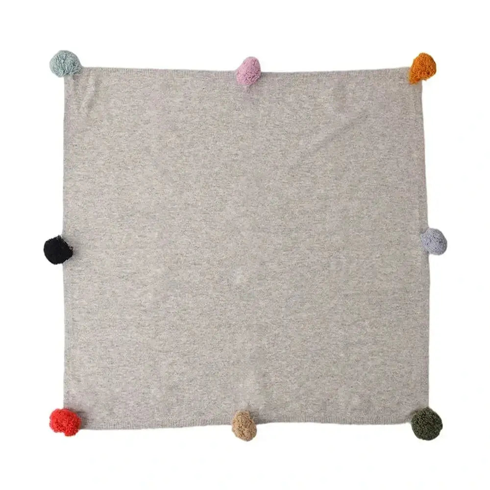 Luxury cashmere throw blanket folded with its colorful pom-pom trim visible