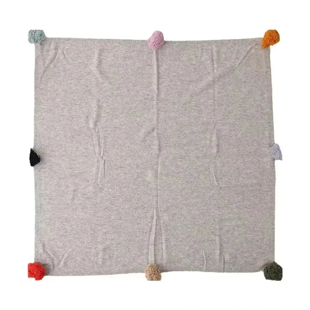 Luxury cashmere throw blanket with colorful pom-poms for a cozy feel.