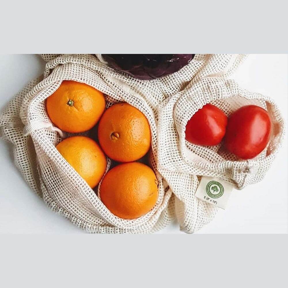 Organic cotton produce bags filled with fresh oranges and tomatoes for eco-friendly shopping.